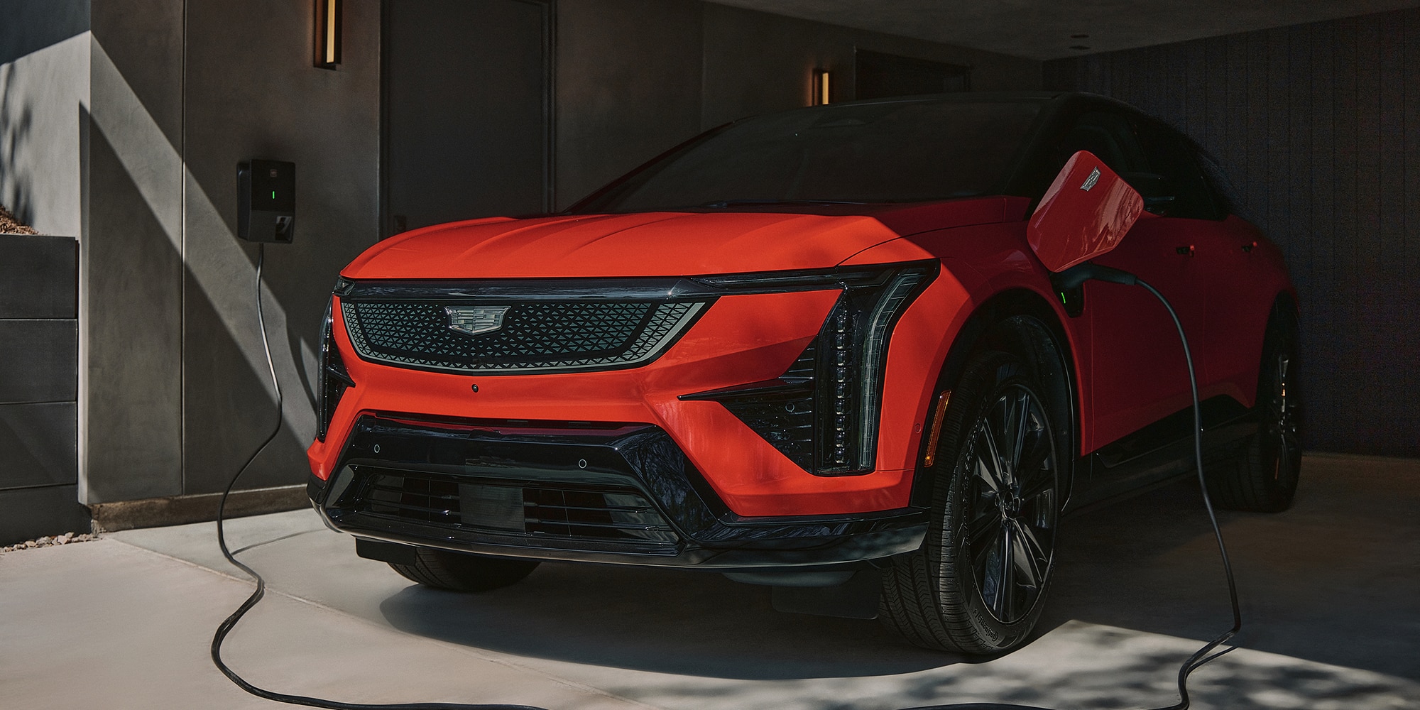 Cadillac OPTIQ 2027 en color Radiant Red circulando por una avenida Cadillac OPTIQ 2027 conectado a una estación de carga eléctrica